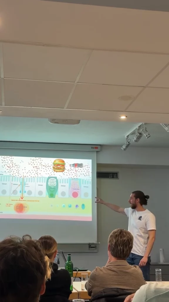 Niclas Reiber zeigt während eines Vortrags zur entzündungshemmenden Ernährung seitlich auf eine Präsentationsfolie, aufgenommen aus der Perspektive der Zuhörer